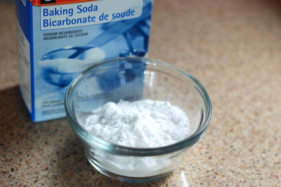 A small glass bowl of white powder next to a blue box of baking soda