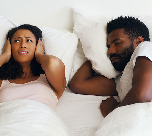 woman covering her ears as her sleeping husband snores