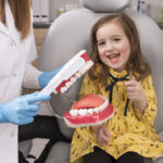 dental anxiety, photo of young girl smiling in dental chair, brushing a dental model of teeth