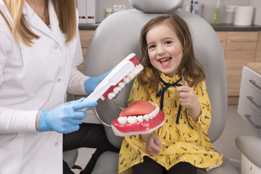 dental anxiety, photo of young girl smiling in dental chair, brushing a dental model of teeth